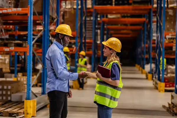 stock image Male and female warehouse workers shaking hands, promoting gender equality and teamwork in the workplace.