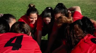 Kırmızı formalı neşeli bir bayan futbol takımı maçtan önce coşku ve takım ruhu göstererek bir araya gelir..