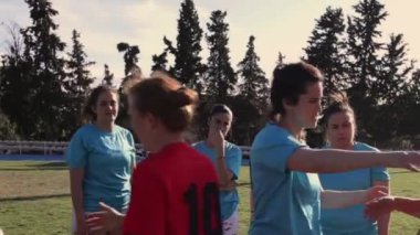İki bayan rugby oyuncusu sahada duygusal bir kucaklaşmayı paylaşıyor ve takım arkadaşları arka planda gözlemliyor..