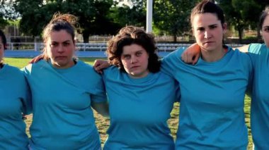  Mavi formalı bayan rugby oyuncuları, maç öncesi kararlılık ve birlik göstererek kol kola dururlar..