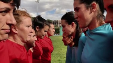 Kırmızı ve mavi formalı bayan rugby oyuncuları maçtan önce odaklanma ve kararlılık göstererek karşı karşıya geliyorlar..