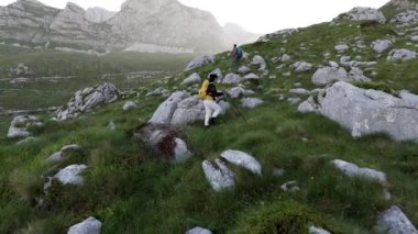 Sırt çantaları ve yürüyüş direkleriyle iki yürüyüşçü kayalık bir dağ yoluna tırmanıyor..