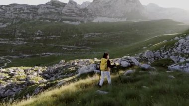 Yürüyüş direkleri ve sırt çantaları olan iki yürüyüşçü gün doğumunda kayalık bir yamaçta geziniyorlar..