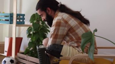 30 'lu yaşlarda sakallı bir adam protez bacaklı, rahat bir evde oturur ve bitkilerle gülümser..