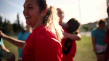 Kadın futbol takımı üyeleri, galibiyet maçından sonra takım çalışmalarını ve başarılarını kutlayarak kucaklıyor ve gülümsüyor..