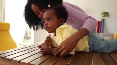 Gülümseyen anne, meraklı kızıyla ahşap bir masada neşe ve sevgi dolu bir etkileşim yakalar..