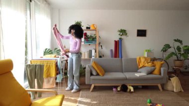 Bir anne, parlak bir oturma odasında çamaşır katlarken meraklı çocuğu kanepenin altını keşfediyor ve günlük hayatın samimi bir anını yakalıyor..