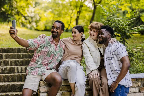 stock image Two multiracial, middle-aged couples smile and pose for a group selfie while sitting on the stairs of a terrace