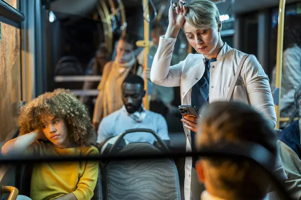 stock image A group of tired passengers, including a female doctor going to the hospital by bus, is checking her smart phone at night, showing the tiredness of a long day.