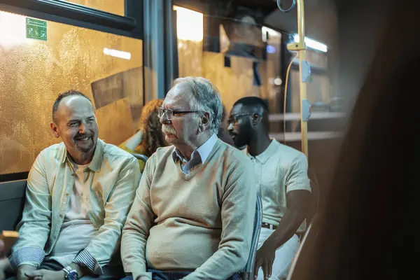 stock image Two men, one elderly and one middle-aged, enjoying a conversation while seated on a bus during an evening commute.