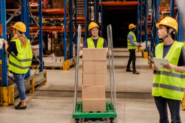 Warehouse workers in safety gear managing inventory and transporting boxes on trolleys, ensuring efficient stock handling. clipart