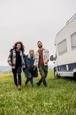 Bir karavanın yanında neşeyle yürüyen üç arkadaş grubu, doğa yolculuğunun tadını çıkarıyorlar..