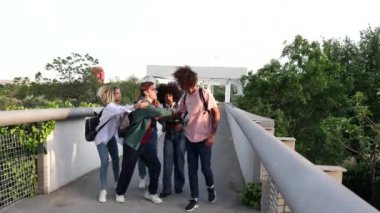 Bir grup öğrenci okuldan sonra kavga ediyor, köprüde duruyorlar, sırt çantaları ve günlük giysiler giyiyorlar..