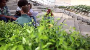 Çok ırklı bir grup öğrenci açık havada birlikte çalışıyor, ortak bir ortamda belgeler ve fikirler paylaşıyorlar..