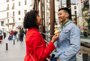 Meşgul bir caddede gülerken taze meyve şişi yiyen mutlu çift..