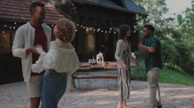 İki çift açık havada dans ediyor, etrafları sicim ışıkları ve kırsal bir ortam ile çevrili, romantik bir ortam yaratıyorlar..