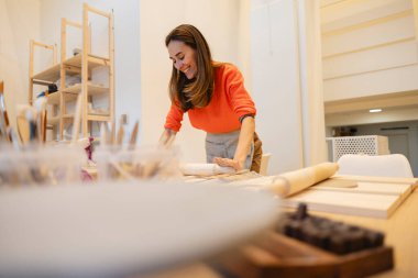 Gülümseyen kadın modern, aydınlık bir mutfakta merdaneyle hamur hazırlıyor..