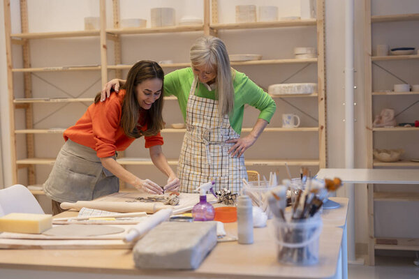 Пожилая женщина, проводящая молодую женщину через технику керамики в дружественной творческой студии.