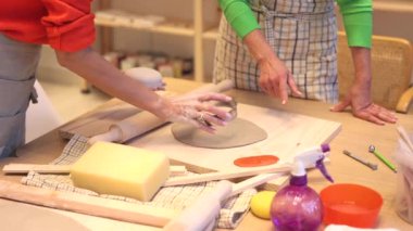 İki kadın masadaki kil levhayı şekillendirmek için araç kullanır, çömlek seansına katılırlar..