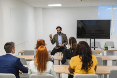 Bir atölye ortamında çeşitli bir ekibin sunumuna öncülük eden işadamı, profesyonel gelişimle meşgul.