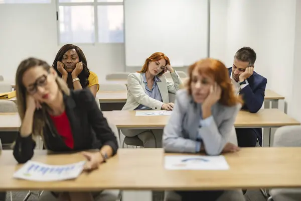 Ofisteki uzun bir atölye çalışmasında çok ırklı iş adamları sıkıntı ve yorgunluk belirtileri gösteriyor..