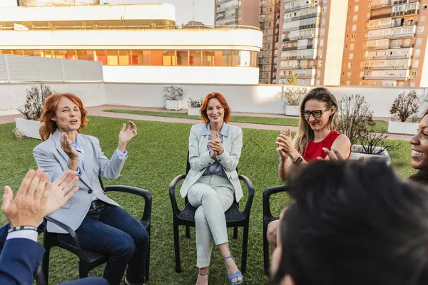 stock image Group of business professionals clapping and participating in a team-building activity outdoors, fostering teamwork and engagement.