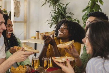 Bir grup mutlu arkadaş pizza dilimlerini paylaşıyor ve birlikte gülüyorlar..