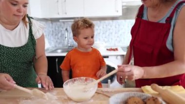 Anne, büyükanne ve genç çocuk mutfakta hamuru karıştırmak ve yuvarlamak için birlikte çalışırlar, aile bağlarının tadını çıkarırlar..