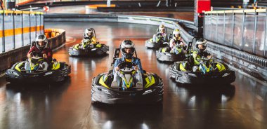 Kasklı genç bir adam kapalı pistte go-kart yarışında bir grup yarışçıyı yönetiyor..