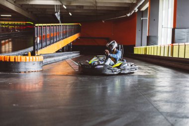 Kask takan sürücü, kapalı bir yarış pistinde go-kart sürüyor ve viraja odaklanıyor..