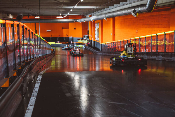 Несколько гонщиков маневрируют через изгиб на крытом треке, светящимся ярко-оранжевым светом.