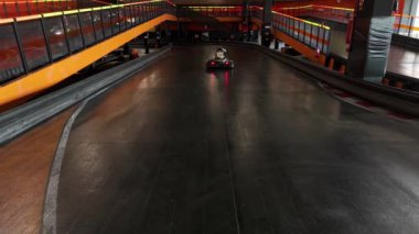 Parlak turuncu korkuluklar ve neon ışıklarla çevrili kapalı bir pistte yol alan tek bir go-kart sürücüsü var..