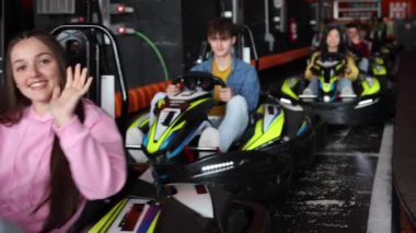 Go-kart kullanan, el sallayan ve gülümseyen, eğlenceli bir yarış deneyimi için hazır bir grup genç..