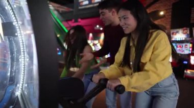 Bir grup arkadaş renkli bir eğlence mekanında gülümseyen ve odaklanan bir oyun oynuyorlar..