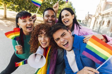 Neşeli ve çeşitli arkadaşlar ellerinde gökkuşağı bayrakları ve megafonla LGBTQ Gururunu kutluyorlar..