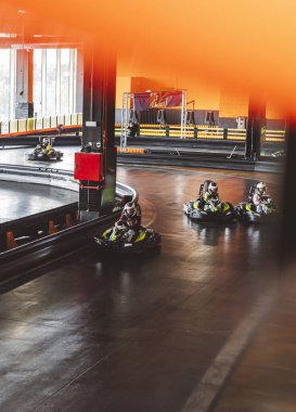 Go-kart sürücüleri kapalı pistte, kasklar ve güvenlik teçhizatlarıyla keskin virajlarda ilerliyorlar..