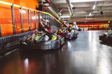 Go-kart sürücülerinin kapalı pistte bir virajda yarışması, odaklanmaları ve kask takmaları..