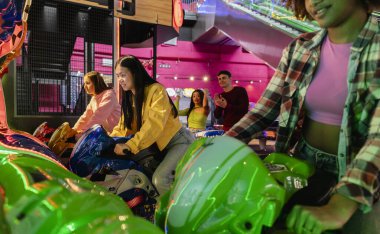 Bir grup arkadaş, canlı neon ışıkları ve odaklanmış ifadeleriyle bir atari motorsiklet yarışı oyununa katıldılar..