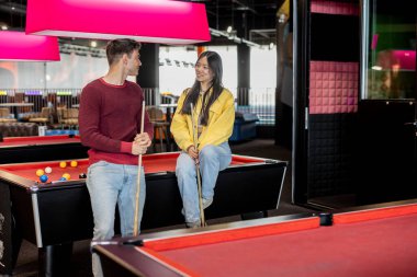 İki arkadaş oyun sırasında bilardo masasının yanında ıstaka tutarken gevşeyip sohbet ediyorlar..