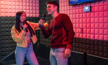 İki arkadaş karaoke seansında eğleniyor, mikrofon tutuyor ve renkli bir odada gülücüklerle şarkı söylüyor..