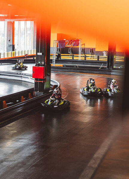 Водители картинга бегут по крытой трассе, перемещаясь по острым поворотам со шлемами и защитным снаряжением..