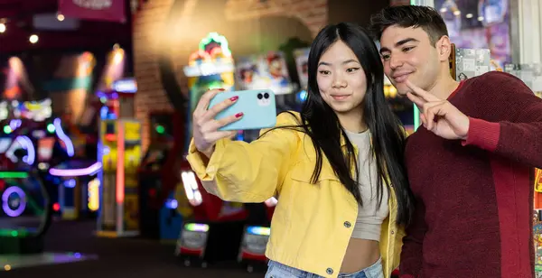 stock image Two friends take a selfie together in a vibrant arcade, posing with smiles and a peace sign.