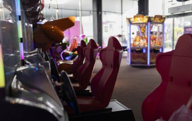 Parlak neon ışıkları ve arka planda atari makineleri olan loş ışıklı atari salonunda boş yarış simülatörü koltukları. Bir atari salonunda Boş Yarış Oyunları Koltukları
