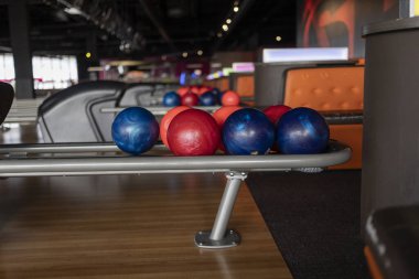 A close-up view of colorful bowling balls on a rack in a dimly lit modern bowling alley. clipart