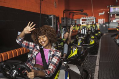 Smiling young adults in go-karts ready for an exciting race at an indoor track. clipart