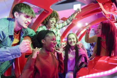 Dostlar Arcade Yarış Oyunu 'nda tezahürat yapıyor ve kutlama yapıyor, bir grup arkadaş heyecanlı bir şekilde zaferi kutluyor ve atari yarışı oynuyorlar, birlikte heyecanın tadını çıkarıyorlar..