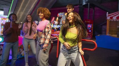 Dans eden ve Arcade 'de eğlenen arkadaşlar, dans eden ve oyun salonunda eğlenen bir grup genç arkadaş, gülümseyerek ve tezahürat yaparak.