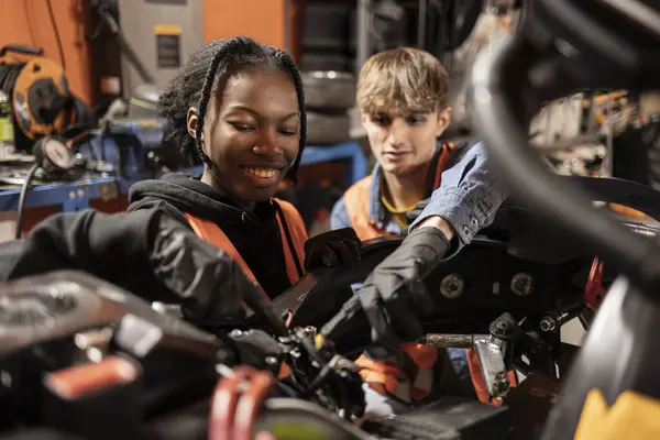 stock image Two young mechanics, one male and one female, working together on engine repairs in a garage, wearing safety vests. Diverse Young Mechanics Working on Engine in Garage