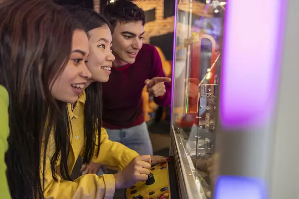 Arcade 'de heyecanlı bir şekilde pençe oyunu oynuyorlar. Bir grup genç arkadaş hevesle pençe makinesiyle oynuyorlar, renkli bir oyun salonunda odaklanmış ve heyecanlılar..