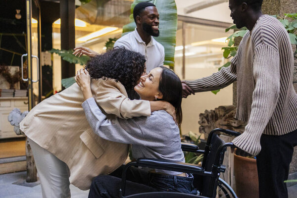 Diverse group of friends happily embracing outdoors, including a woman in a wheelchair, sharing a joyful moment. Group of friends embracing and smiling in an outdoor setting
